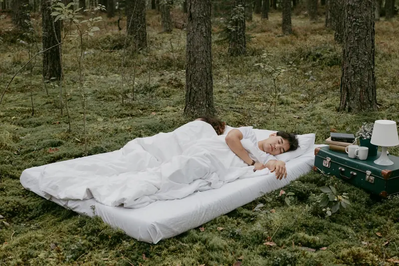 A couple peacefully sleeping on a mattress in a forest setting, capturing a serene outdoor camping vibe