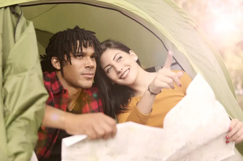 A happy couple inside a tent enjoying an outdoor camping trip, looking at a map together