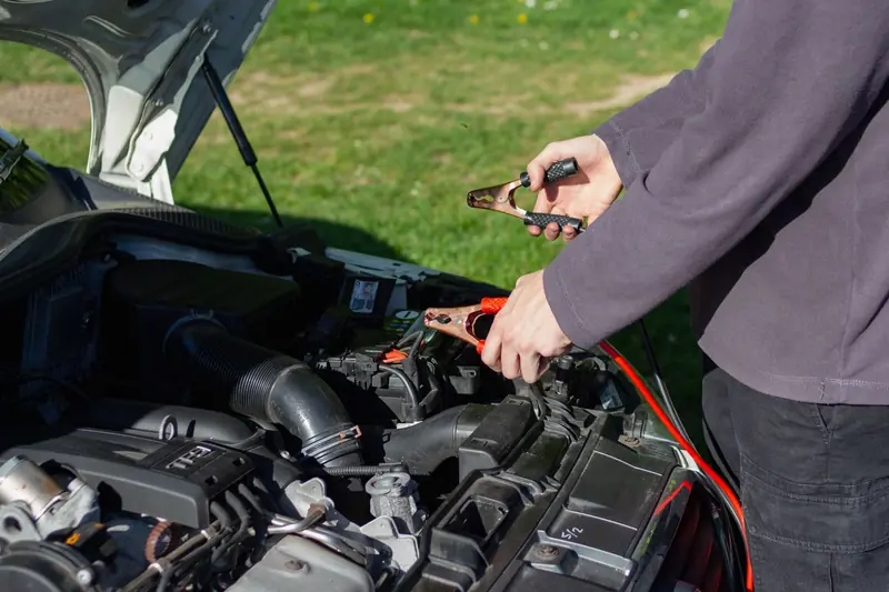 Close-up of mechanic using jumper cables to jump-start a car battery outdoors