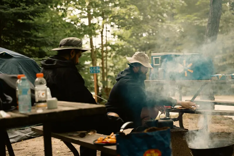Outdoor camping scene with men cooking at a campsite with tents and trees
