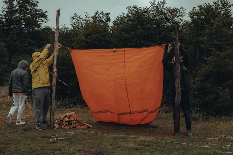 Group of people setting up an orange tarp in a forested camping area