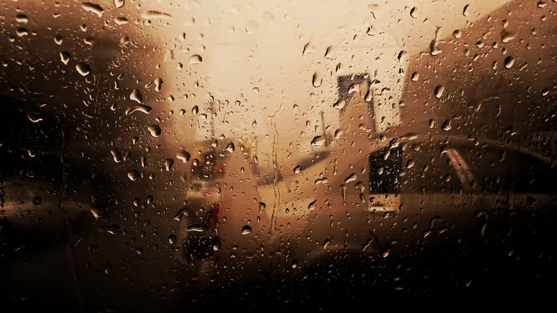 Artistic view of raindrops on a car window with blurred vehicles in the background, creating a moody atmosphere