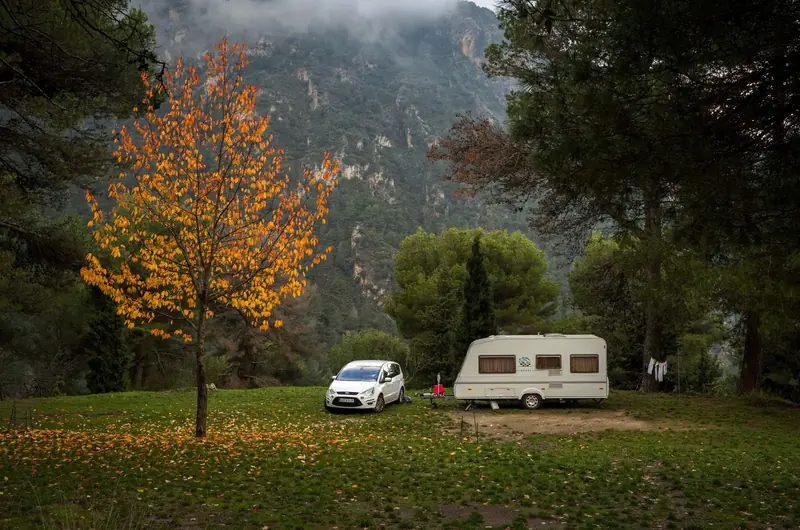 Cozy camping scene in Salobreña, Spain with a car, trailer, and autumn foliage