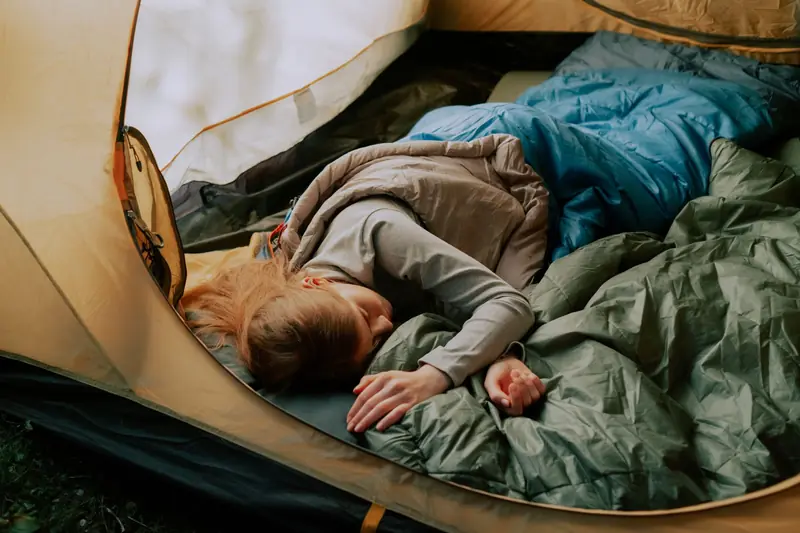 A serene scene of a woman sleeping comfortably in a tent during a camping trip, surrounded by nature