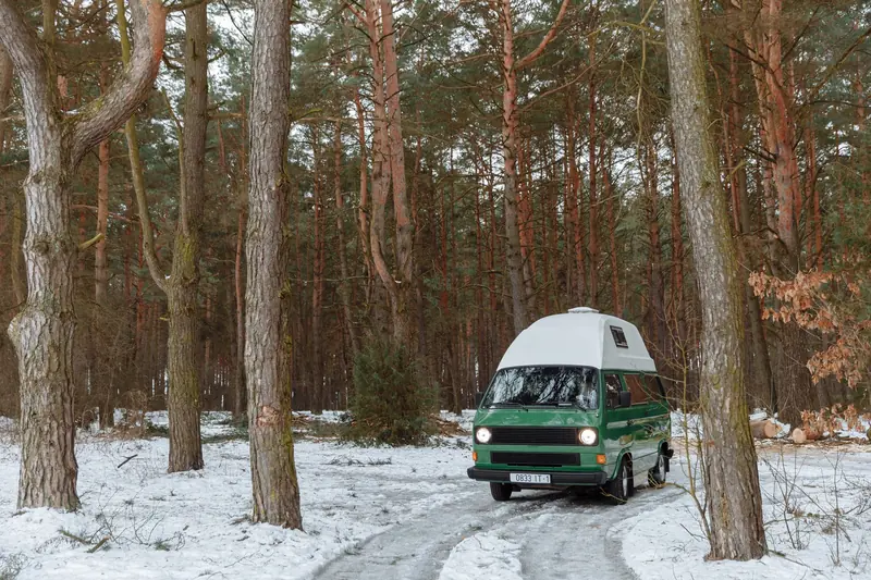 Vintage campervan parked in a snowy forest, encapsulating a serene winter camping vibe