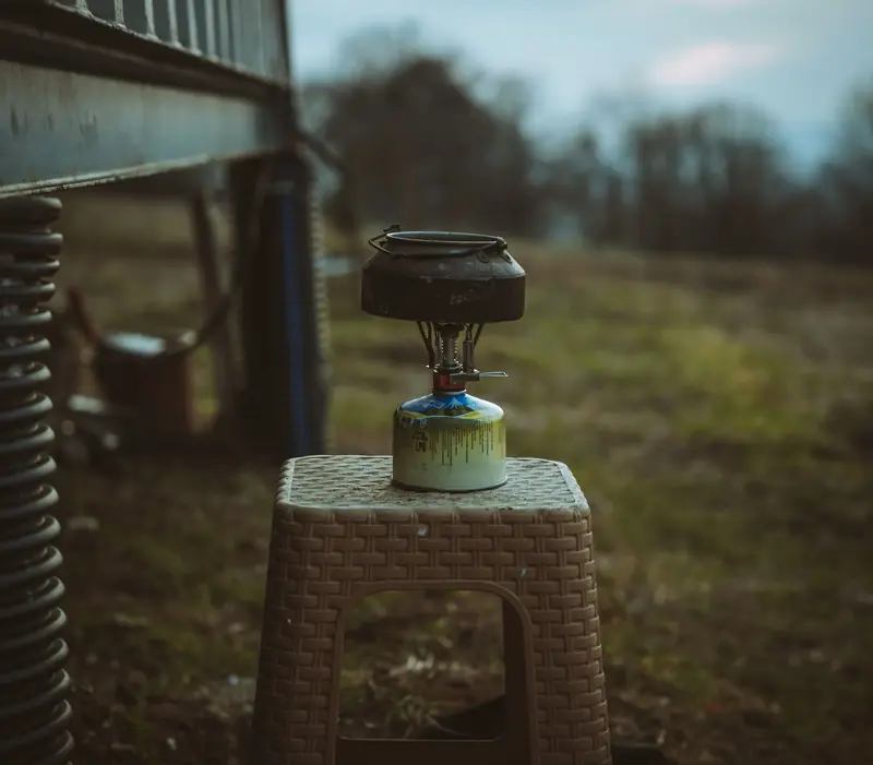 Close-up of a camping stove on a stool in a rural outdoor field setting