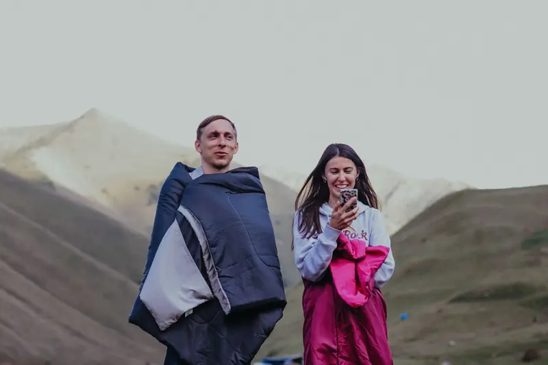 A man and woman wrapped in sleeping bags enjoying nature and outdoor camping in mountainous terrain