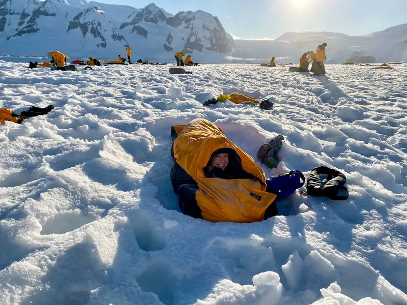 Smiling woman in a sleeping bag during a camping expedition on Antarctica's snowy terrain