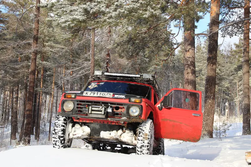 Offroad red SUV driving through a snowy forest during winter