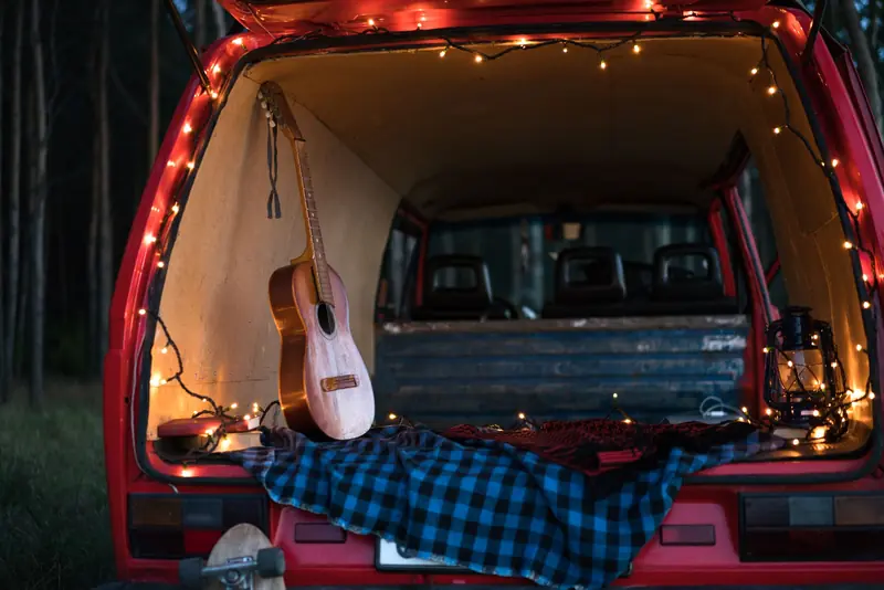 A serene camping scene with an acoustic guitar and lights in a car trunk, perfect for music lovers